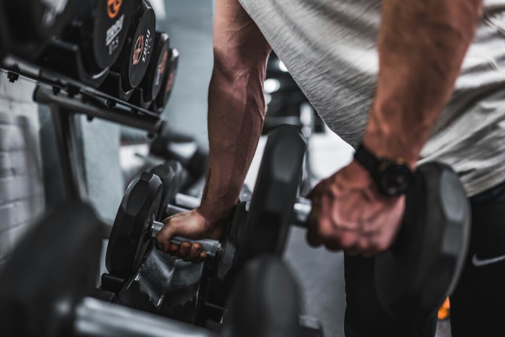 Krafttraining ab 40: Hände greifen im Fitnessstudio nach zwei Kurzhanteln am Hantelständer
