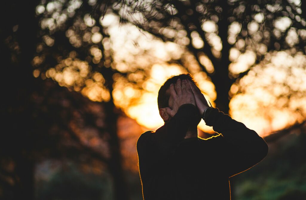 Erschöpfter Mann im Gegenlicht bei Sonnenuntergang fasst sich an den Kopf – trainieren trotz Stress richtig dosieren