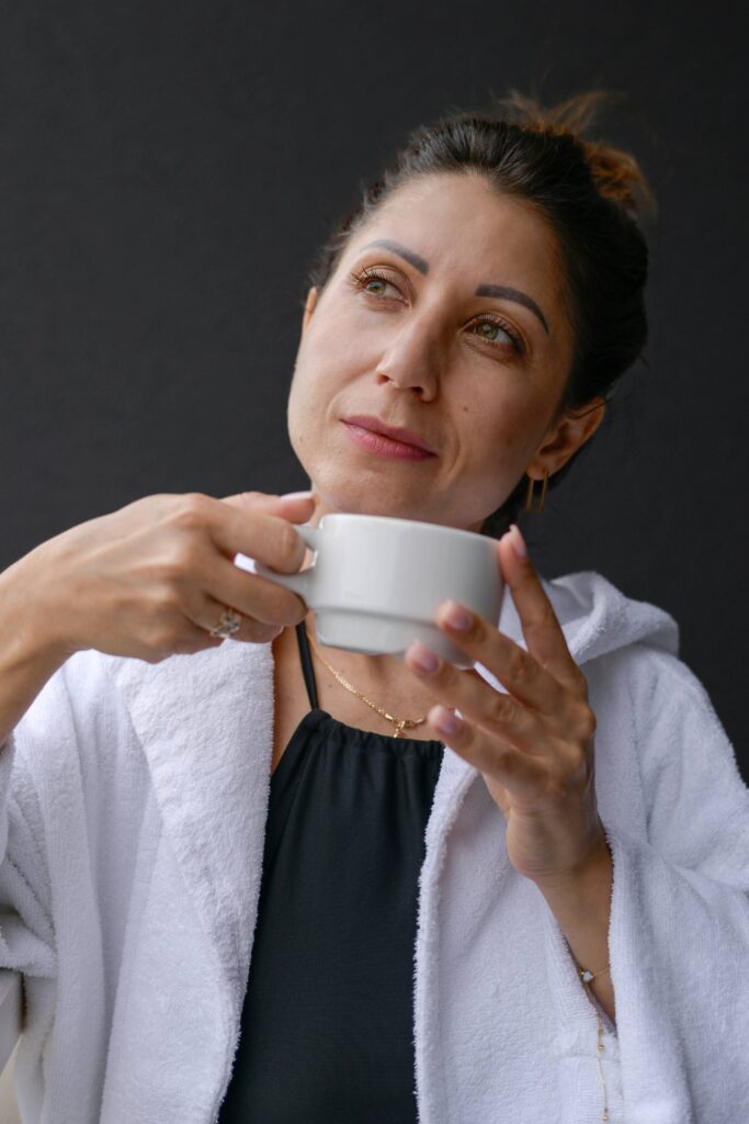 Abnehmen in den Wechseljahren: Frau um die 40 im weißen Bademantel hält nachdenklich eine Tasse in beiden Händen